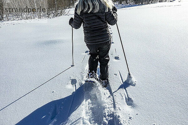 USA  Idaho  Ketchum  Rückansicht einer älteren Frau beim Schneeschuhwandern in einem schneebedeckten Feld