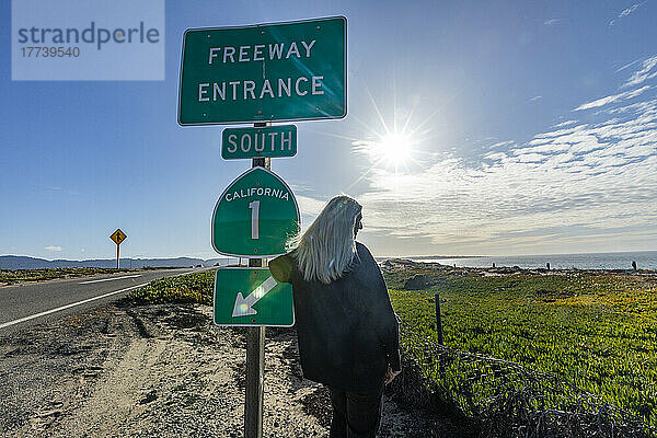 USA  Kalifornien  Carmel  Rückansicht einer älteren blonden Frau am Ortseingangsschild des Highway 1