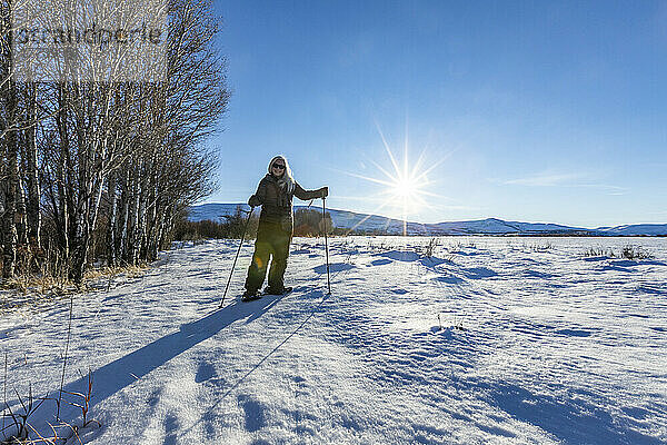 USA  Idaho  Bellevue  ältere blonde Frau beim Schneeschuhwandern in schneebedeckter Landschaft an einem sonnigen Tag