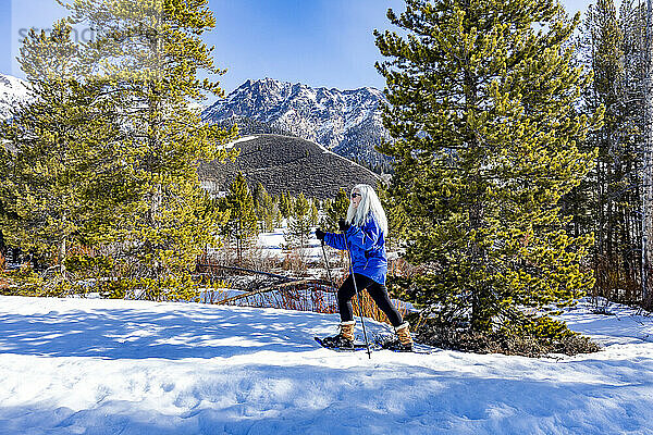 USA  Idaho  Ketchum  ältere blonde Frau beim Schneeschuhwandern in einer schneebedeckten Landschaft