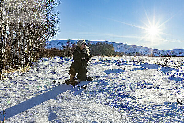 USA  Idaho  Bellevue  Ältere blonde Frau mit Schneeschuhen blickt an einem sonnigen Tag auf die schneebedeckte Landschaft