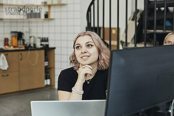 Lächelnde Unternehmerin mit Hand am Kinn im Büro während einer Besprechung