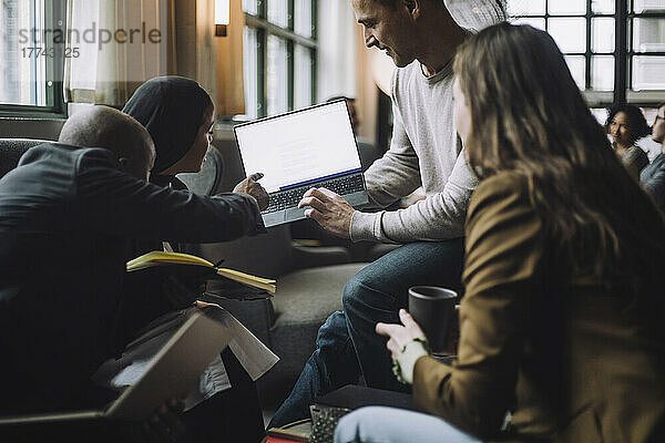 Geschäftsmann zeigt auf Laptop  während er Kollegen im Kreativbüro erklärt