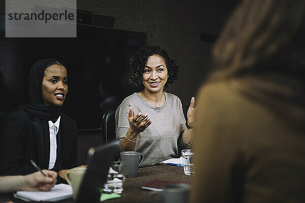 Lächelnde reife Frau gestikuliert beim Austausch von Ideen mit Kollegen während einer Besprechung im Kreativbüro
