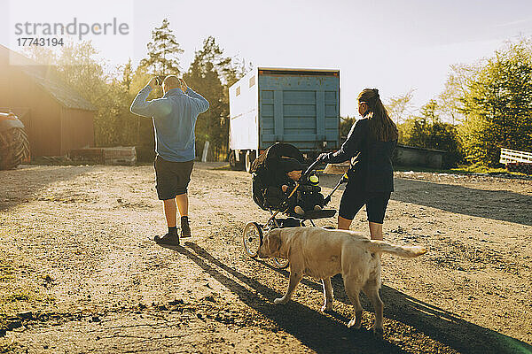 Eltern mit männlichem Kleinkind gehen an einem sonnigen Tag mit Hund spazieren