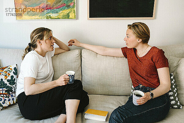 Lesbisches Paar im Gespräch beim Kaffee auf dem Sofa im Wohnzimmer zu Hause