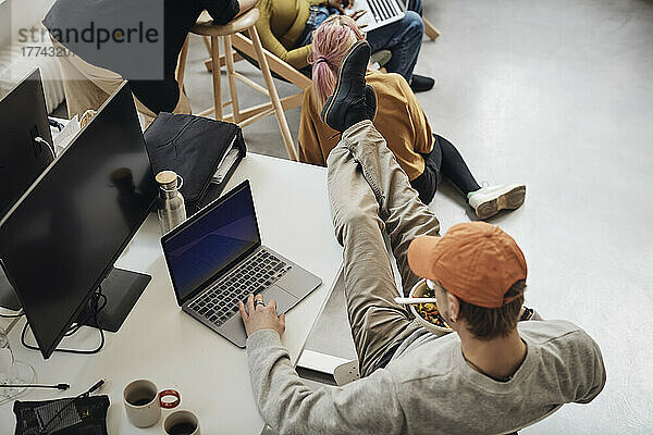 Hohe Winkel Ansicht der männlichen Programmierer mit Füßen auf dem Schreibtisch mit Laptop während des Essens Mittagessen im Büro