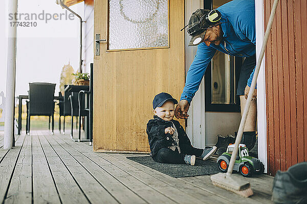 Lächelnder Vater spielt mit seinem auf der Fußmatte sitzenden Sohn auf der Veranda