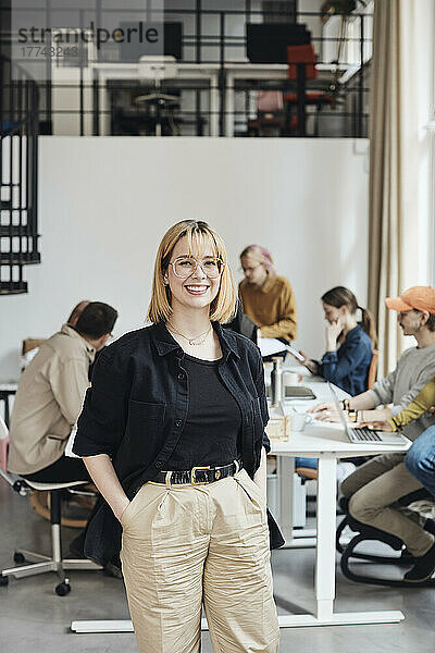 Porträt einer selbstbewussten Geschäftsfrau mit Händen in den Taschen  die in einem Büro eines Start-ups steht