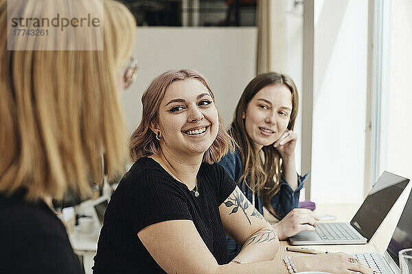 Lächelnde Unternehmerinnen  die einen Kollegen während einer Besprechung im Büro ansehen