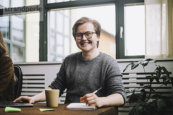 Porträt eines glücklichen männlichen Unternehmers mit Brille  der am Konferenztisch sitzt