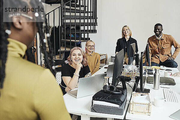 Lächelnde Kollegen  die eine Geschäftsfrau während einer Besprechung im Büro ansehen