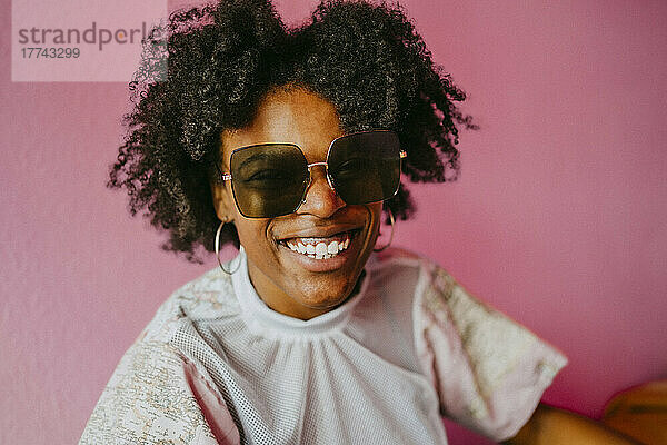 Glückliche Hipster-Frau mit Sonnenbrille vor rosa Wand zu Hause
