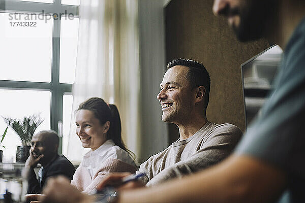 Glücklicher reifer männlicher Unternehmer  der während einer Besprechung im kreativen Bereich neben seinen Kollegen sitzt