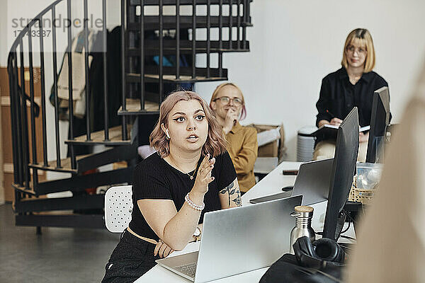 Junge weibliche Computerprogrammiererin im Gespräch mit einem Kollegen während eines Geschäftstreffens im Büro