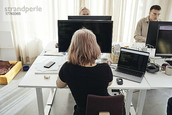 Rückansicht einer Geschäftsfrau  die an einem Computer arbeitet  während sie am Schreibtisch im Büro sitzt