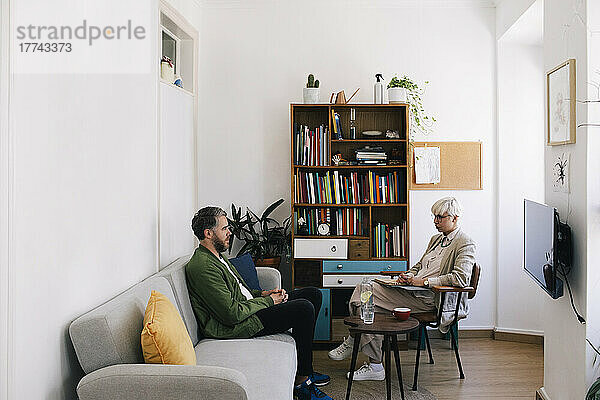 Weibliche Psychotherapeutin im Gespräch mit einem männlichen Patienten  der auf dem Sofa im Therapiebüro sitzt
