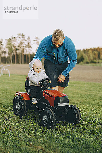 Vater fährt seinen Sohn im Spielzeugtraktor auf dem Bauernhof mit