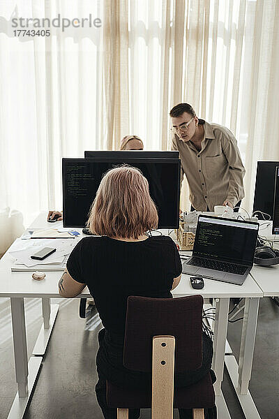 Geschäftsfrau mit Computer am Schreibtisch  während Kollegen im Büro diskutieren
