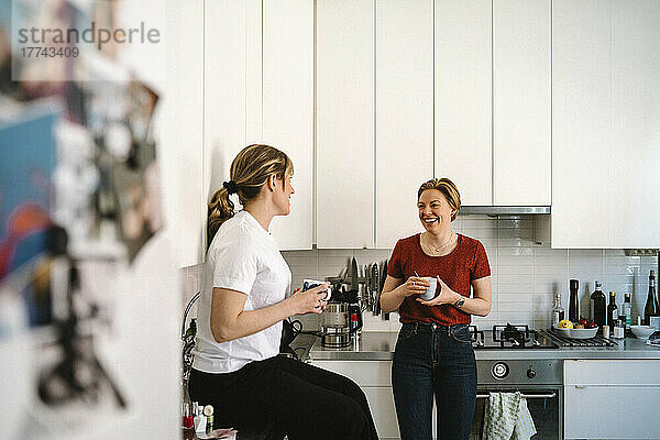 Glückliches lesbisches Paar im Gespräch beim gemeinsamen Kaffee in der Küche zu Hause