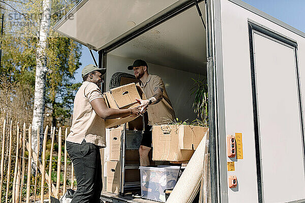 Multirassische Umzugshelfer entladen an einem sonnigen Tag Kartons vom Lastwagen
