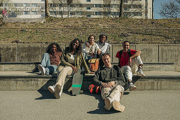 Lächelnd multirassische männliche und weibliche Freunde sitzen zusammen im Park an einem sonnigen Tag