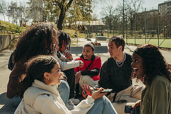 Multirassische männliche und weibliche Freunde unterhalten sich beim Zusammensitzen im Park
