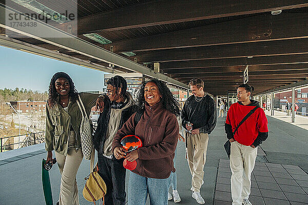 Männliche und weibliche Freunde verschiedener Rassen gehen zusammen unter einer Brücke am Bahnhof