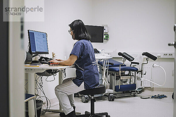 Seitenansicht einer Ärztin  die einen Desktop-PC am Schreibtisch in einer medizinischen Klinik benutzt