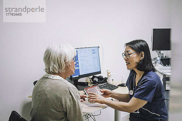 Reife Ärztin diskutiert mit älterem Patienten im Krankenhaus über Pillenorganisator