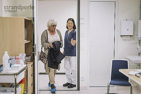 Lächelnder Arzt gestikuliert zu einem älteren Patienten  der sein Büro im Krankenhaus betritt