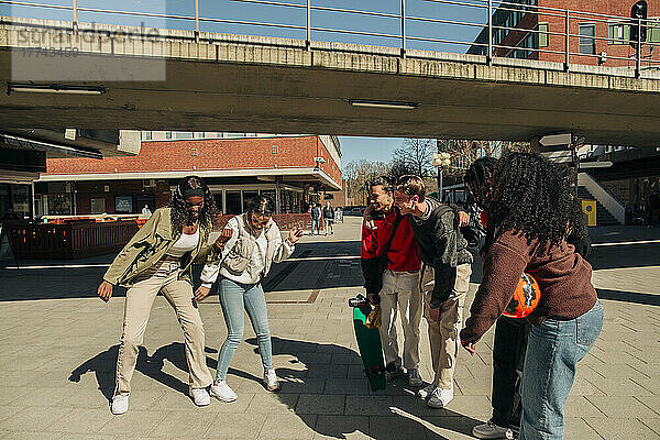 Multirassische Freunde beobachten junge Frauen  die an einem sonnigen Tag auf der Straße zusammen tanzen
