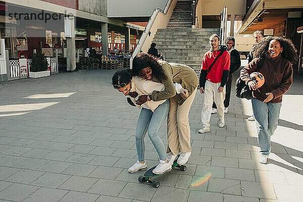 Verspielte Freundinnen stehen auf einem Skateboard auf der Straße