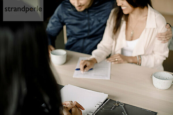Immobilienmakler mit Ehepaar bei der Vertragsunterzeichnung am Tisch im neuen Haus