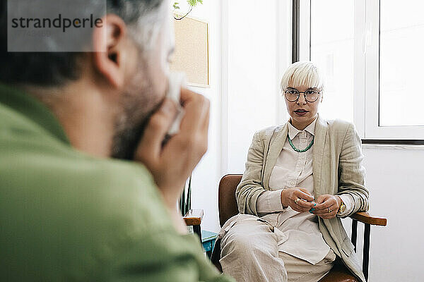 Weibliche Psychotherapeutin bespricht sich mit einem männlichen Patienten  der im Therapiebüro sitzt