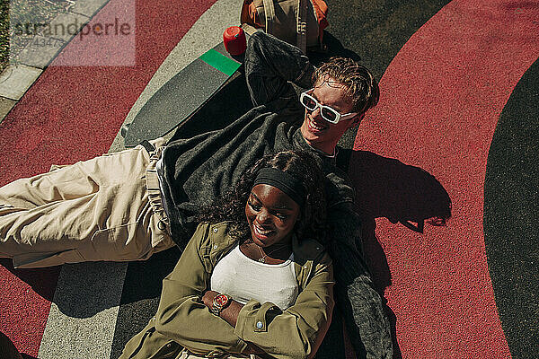 Multirassischer junger Mann und Frau liegen auf einem Spielplatz an einem sonnigen Tag
