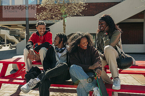 Glückliche multirassische junge Freunde unterhalten sich auf einer Bank sitzend