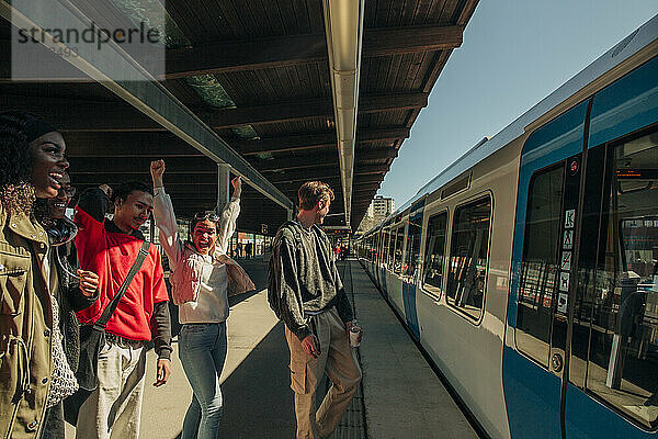 Fröhliche multirassische Freunde  die sich über die Ankunft eines Zuges am Bahnhof freuen
