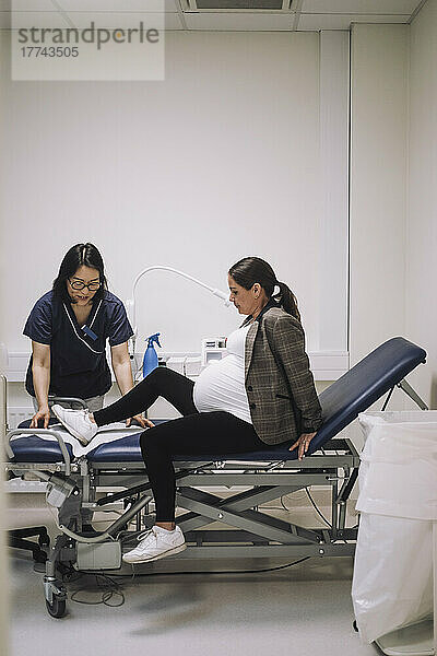 Schwangere Frau sitzt auf der Trage eines Arztes in einer medizinischen Klinik