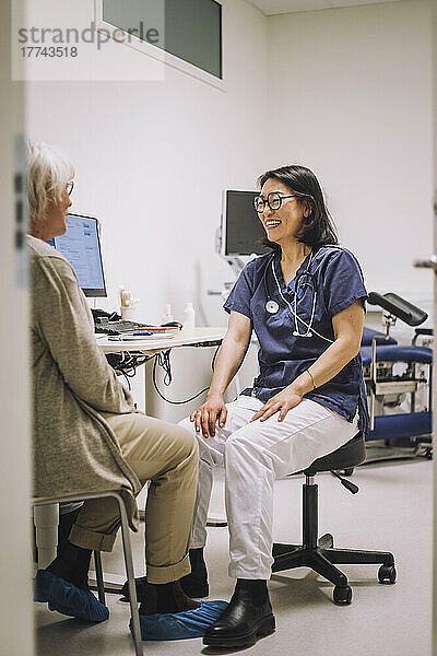 Glückliche Ärztin in voller Länge im Gespräch mit einer älteren Frau in einer medizinischen Klinik
