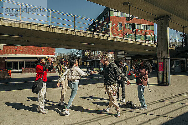 Gemischtrassige Freunde applaudieren einem jungen Mann und einer Frau  die an einem sonnigen Tag auf der Straße tanzen