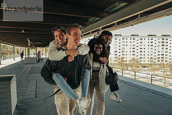 Multirassische verspielte Freunde  die sich am Bahnsteig gegenseitig Huckepack nehmen