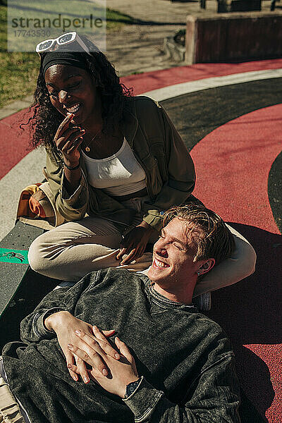 Lächelnder Mann  der auf dem Schoß seiner Freundin liegt und sich auf einem Spielplatz an einem sonnigen Tag entspannt
