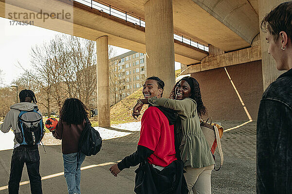 Seitenansicht von fröhlichen multirassischen Freunden  die gemeinsam unter einer Brücke spazieren gehen