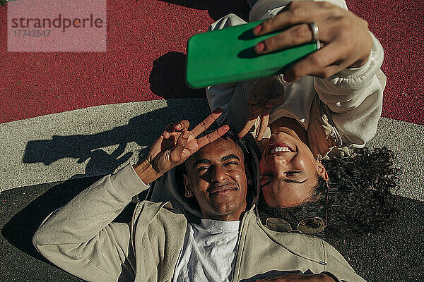 Freunde machen ein Friedenszeichen  während sie ein Selfie mit ihrem Smartphone auf einem Spielplatz machen
