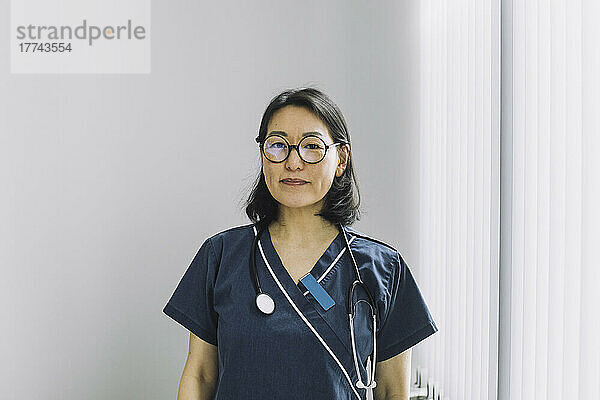 Porträt einer Ärztin mit Brille an einer weißen Wand in einer medizinischen Klinik