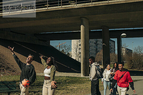 Multirassischer junger Mann und Frau singen  während Freunde in der Stadt an einem sonnigen Tag spazieren gehen