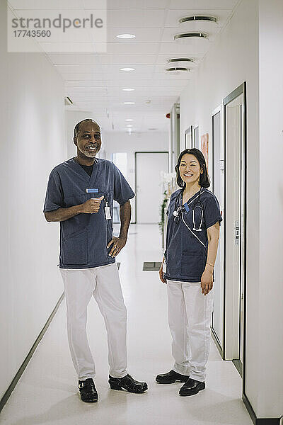 Ganzkörperporträt eines lächelnden Mannes und einer lächelnden Frau  die in einer medizinischen Klinik im Flur stehen