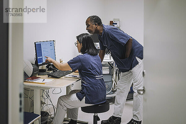 Eine Ärztin zeigt auf einen Computerbildschirm  während sie mit einem männlichen Kollegen im Krankenhaus diskutiert