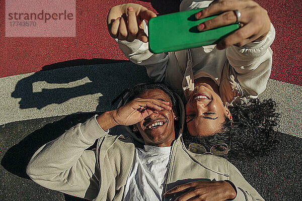 Glückliche junge Freunde nehmen Selfie durch Smartphone  während in Spielplatz liegen